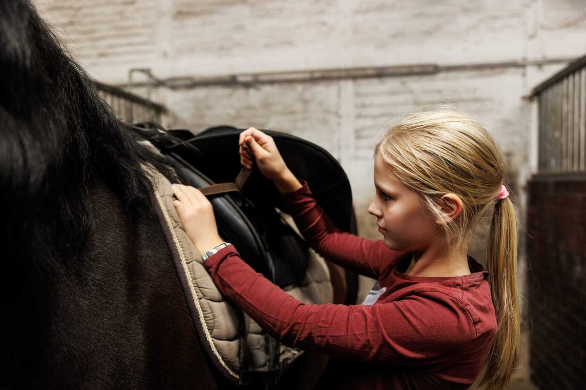 Teenage girl adjusting horse tack