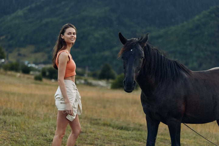 Woman standing in grassy field beside horse